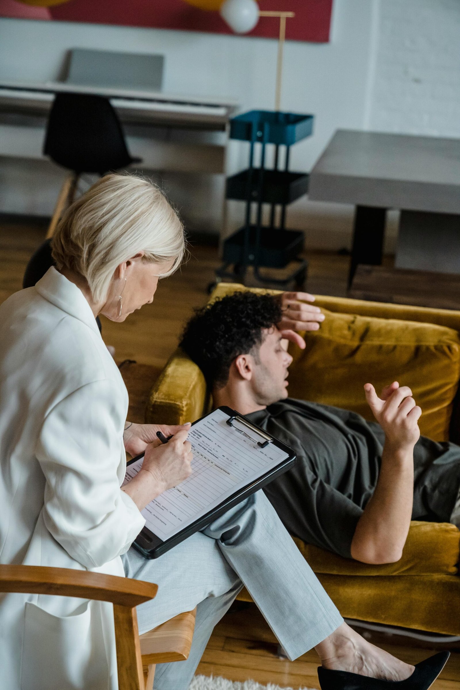 A psychologist taking notes during a therapy session with a patient lying on a couch.